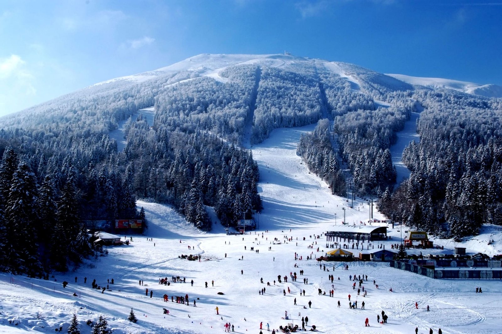 Skiers on the snow-covered slopes of Bjelašnica mountain above Sarajevo under a clear blue sky