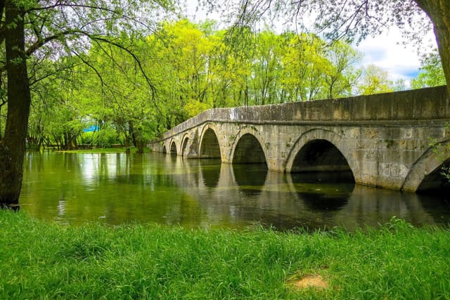 The stone arches of the Roman Bridge reflected in the Bosna River at Ilidža